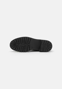 Semelle de botte en caoutchouc noir avec des crampons profonds pour une meilleure adhérence, présentant une surface lisse et des motifs en forme de diamant pour la prise.