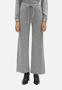 Pantalones de chándal grises, de pierna ancha, con cintura ajustable y textura suave, combinados con botas de tacón negras para aportar contraste.