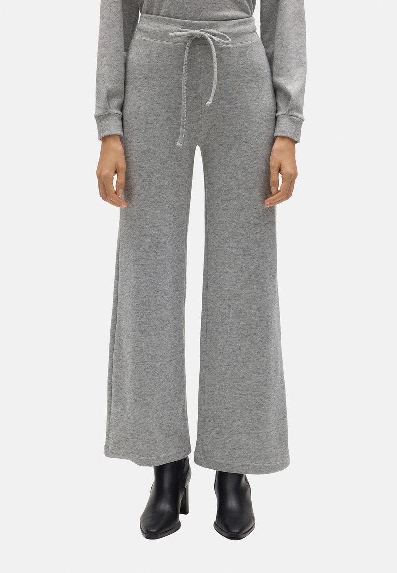 Pantalones de chándal grises, de pierna ancha, con cintura ajustable y textura suave, combinados con botas de tacón negras para aportar contraste.