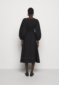 Svart klänning i knästorlek med puffärmar, åtsittande midja och vit sömnadsdetalj i fållen. Tillverkad av ett lätt och slätt tyg.