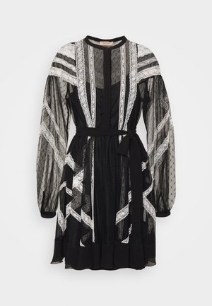 Robe noire en tissu transparent avec manches longues bouffantes, rayures verticales en dentelle blanche et ceinture nouée à la taille sur un fond uni.