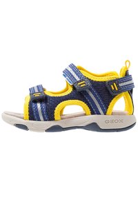 Modré a žluté sandály s prodyšným síťovaným svrchním materiálem, nastavitelnými popruhy a polstrovanou podrážkou. Mají strukturovaný povrch a kulaté otvory.