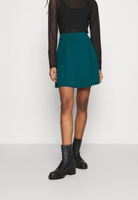 Teal skaterkjol i mjukt material, med plisseringar, matchad med en genomskinlig svart långärmad topp och svarta snörade kängor.