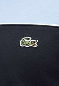 Logo de crocodile vert brodé avec un contour blanc sur un fond de tissu bleu marine et bleu clair.