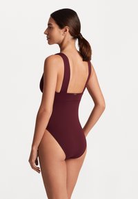 Fato de banho de uma peça bordo com alças largas e costas baixas. Tecido suave e elástico com costuras mínimas e um pequeno detalhe logo metálico.