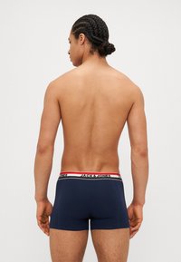 Boxers navy bleu avec une ceinture blanche et rouge arborant le logo "JACK & JONES". Texture lisse, design ajusté et coupe courte.