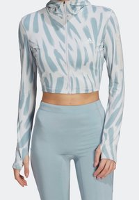 Femme portant un crop hoodie d'entraînement à motif bleu clair et blanc avec des trous pour les pouces et un legging taille haute uni bleu clair.