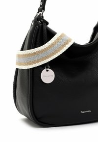 Schwarze Lederhandtasche mit strukturiertem Finish, ausgestattet mit einem gewebten Tragegurt in Grau, Beige und Weiß, sowie einem silbernen runden Etikett mit der Aufschrift "Tamaris."