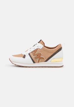 Las zapatillas cuentan con una parte superior tejida de color marrón claro, detalles en cuero blanco y herrajes dorados. Suela plana con un patrón de agarre de goma, diseñada para la comodidad.