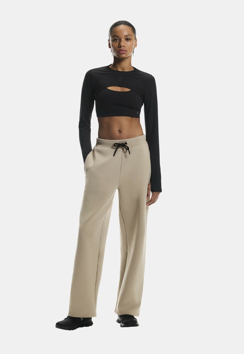 Sort langærmet top med skåret design parret med beige brede bukser, der har en snøre i taljen og en glat tekstur.