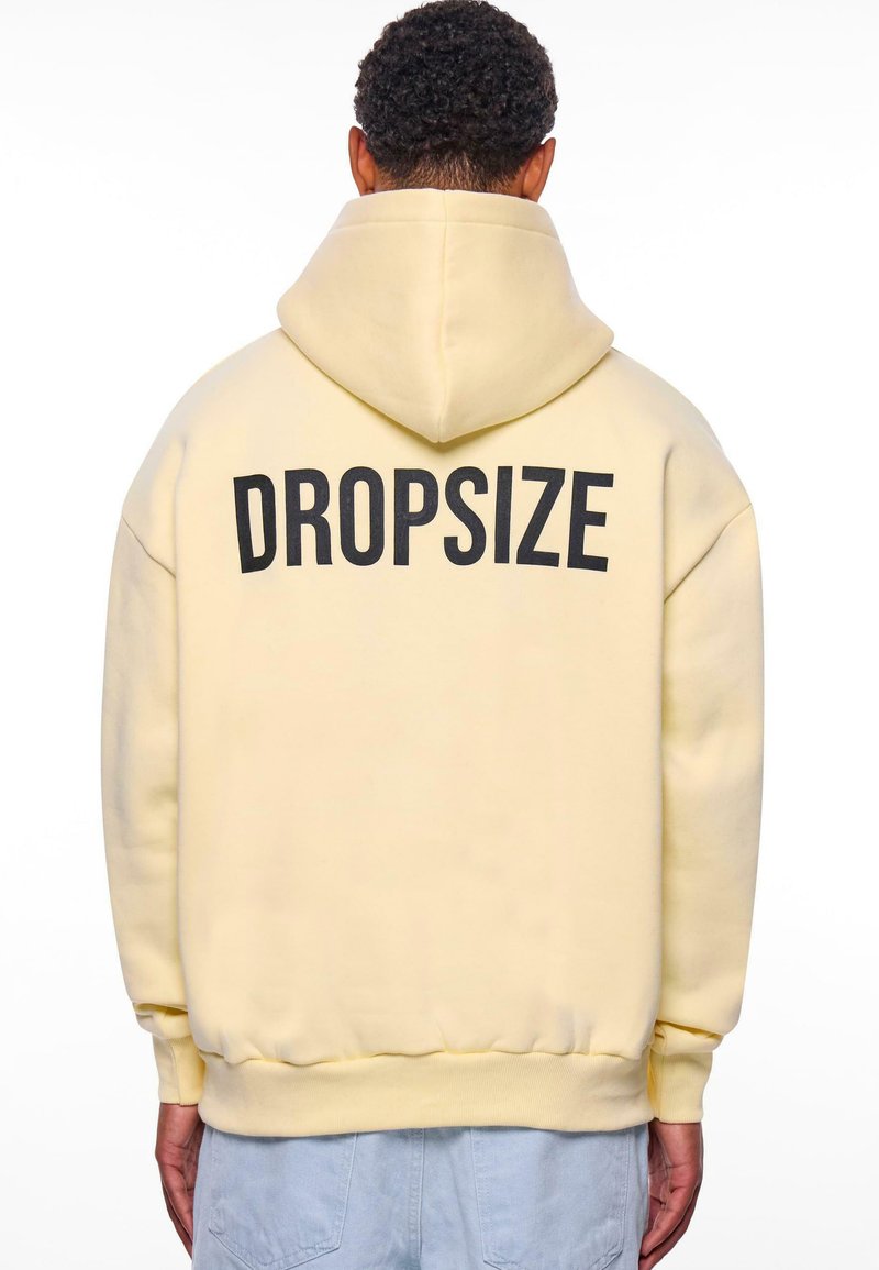 Jasnożółta bluza z kapturem z dużym czarnym napisem "DROPSIZE" na plecach. Posiada kaptur, luźny krój oraz ściągacze na rękawach i u dołu.