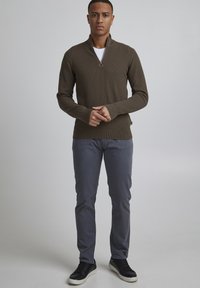 Dark green textured quarter-zip sweater, paired with gray pants and black sneakers. Sweater features a ring pull detail at the collar.