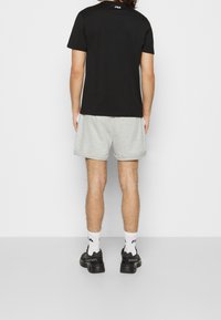 Černé tričko s krátkým rukávem a logem na zádech, doplněné o šedé kraťasy. Celkový vzhled uzavírají černé tenisky a bílé ponožky.