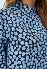 Tessuto nero con un motivo floreale blu, caratterizzato da fiori testurizzati. Design a scollo alto con pieghe sottili, che creano un aspetto strutturato.