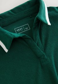 Grön texturerad polo-shirt med vit accentkrage, som har en knapplista med tre knappar och märkesetikett "NEXT ACTIVE" inuti kragen.