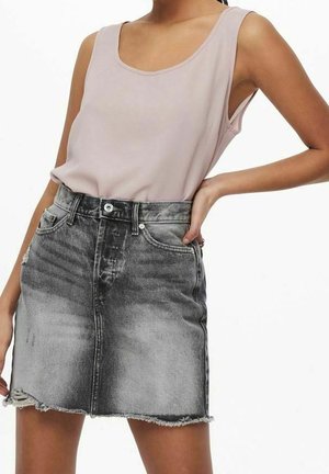 Frau in einem hellrosa ärmellosen Top mit Rundhalsausschnitt, das in einen hochgeschnittenen, ausgebleicht schwarzen Denim-Minirock mit fransendem Saum gesteckt ist.