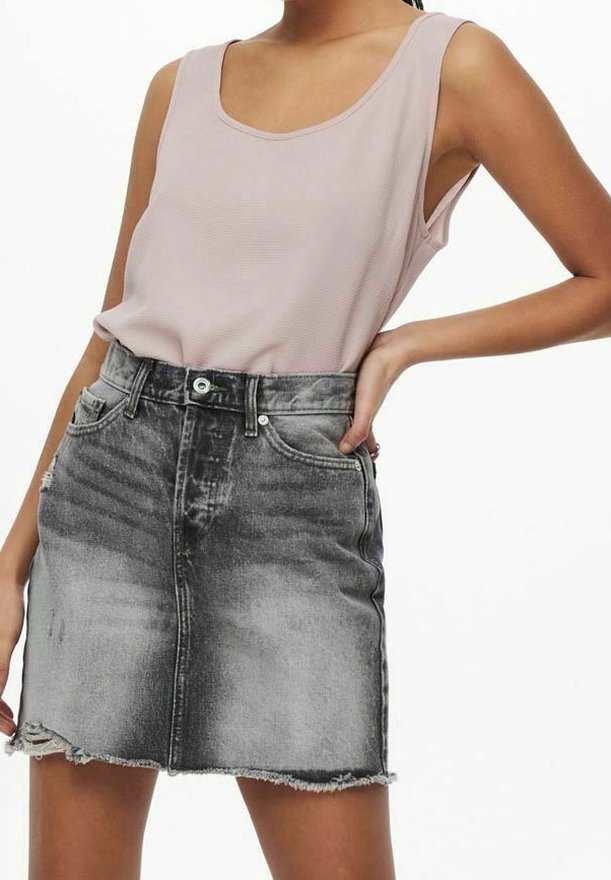 Donna che indossa un top senza maniche color rosa chiaro con scollo a barchetta, infilato in una mini gonna di jeans nera sbiadita a vita alta con orlo sfrangiato.