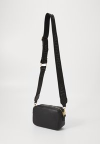 Borsa a tracolla in pelle nera con finitura testurizzata, dotata di una zip dorata e di una tracolla regolabile con logo "VALENTINO" in nero.