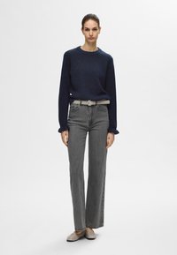 Mörkblå stickad tröja med ribbad rundhals, grå högmidjade raka jeans och beige ballerinas, med ett ljust grått bälte.