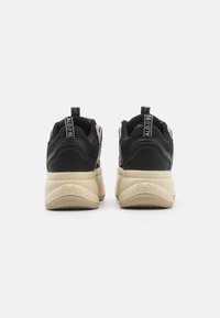 Svarte og beige sneakers med teksturert overdel, polstret krage og bakre trekkstropp. Viser en logo på siden og et mønstret såle.