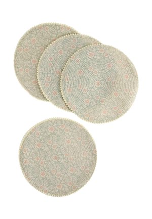 Quattro tovagliette rotonde intrecciate con un delicato motivo floreale in verde pallido e rosa, ciascuna bordata da piccoli pompon di tessuto.