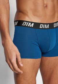 Blaue Baumwoll-Boxershorts mit einem schwarzen Bund, auf dem der weiße Text "DIM." zu sehen ist. Die Nahaufnahme zeigt die gerippte Textur und das figurbetonte Design.