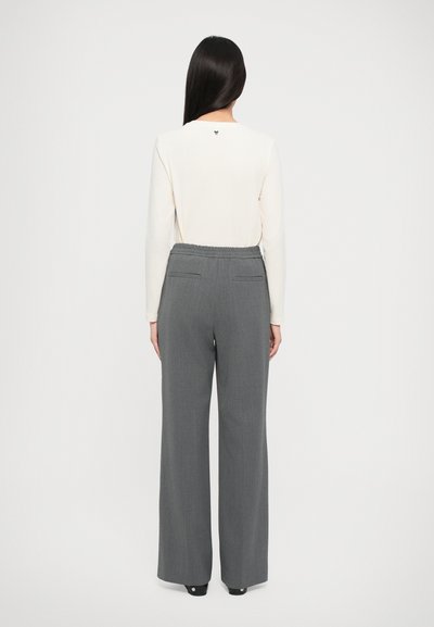 Light cream long-sleeve top with a small logo at the back, paired with wide-leg dark gray trousers featuring back pockets and elastic waist.