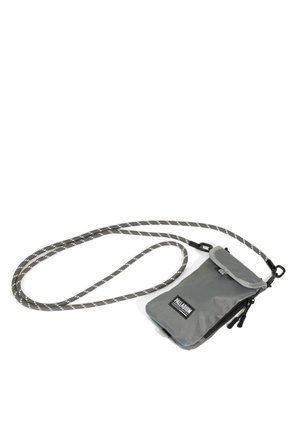 Petit sac bandoulière gris avec fermeture éclair et rabat, marqué "Palladium", fixé à une longue bandoulière en corde rayée gris et blanc.