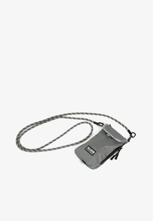 Petit sac bandoulière gris avec fermeture éclair et rabat, marqué "Palladium", fixé à une longue bandoulière en corde rayée gris et blanc.