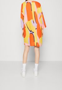 Kolorowa, oversize sukienka z odważnymi abstrakcyjnymi wzorami w kolorach pomarańczowym, żółtym i fioletowym. Wykonana z lekkiego materiału, z rękawami o długości 3/4.
