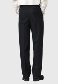 Črne formalne hlače ravnega kroja, z nabranim dizajnom in dvema zadnjima žepoma. Obute z dolgimi rokavi striped srajco in čevlji.