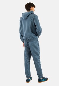 Chándal deportivo para hombre en azul, que incluye una chaqueta con capucha y pantalones con cintura elástica, fabricado en un material suave y ligero con puños elásticos.