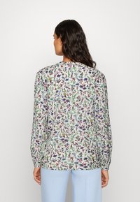 Blusa a maniche lunghe in tessuto leggero con un motivo floreale multicolore su uno sfondo chiaro, con una vestibilità morbida e maniche con polsini.