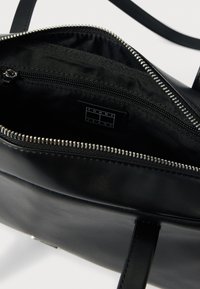 Μαύρη δερμάτινη τσάντα χειρός με κύριο διαμέρισμα με φερμουάρ, φερμουάρ ασημί απόχρωσης και εσωτερικές θήκες. Περιέχει ετικέτα "TOMMY JEANS".