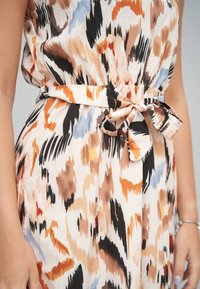 Kangasmekko, jossa on monivärinen, abstrakti kuvio persikan, mustan ja sinisen sävyissä. Mukana kangasvyö, joka sidotaan vyötäröllä, ja pehmeä rakenne.