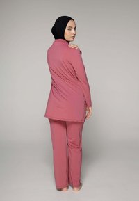 Langsleeve roze tuniek met een lichte staart en bijpassende broek. Lichtgewicht, soepele stof met een minimalistisch ontwerp. Zwarte hijab completeert de outfit.