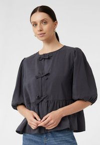 Dunkelgraue Bluse mit gepufften Ärmeln, dekorativen Schleifenverschlüssen und einem Peplum-Saum, aus leichtem Stoff mit glatter Textur.