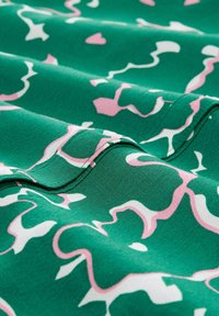 Grüner Stoff mit einer glatten Textur, der ein gewelltes, abstraktes Muster in Pink und Weiß zeigt, mit Falten, die Tiefe und visuelles Interesse schaffen.