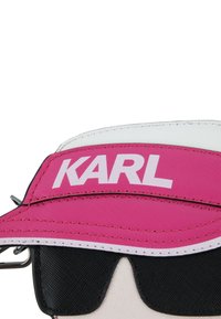 Cappellino visiera rosa con cuciture bianche, caratterizzato da un logo "KARL" in evidenza in carattere bianco. Include occhiali da sole neri con superficie testurizzata.