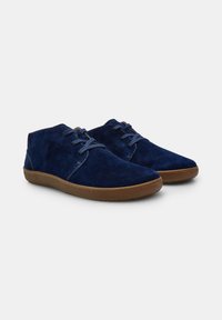 Scarpe in suede blu navy con design a caviglia bassa, punta tonda e chiusura con lacci. Suola in gomma con un accento marrone intorno al bordo.