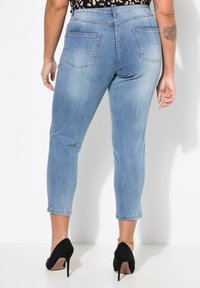 Jeans de denim azul claro con un corte ajustado, longitud recortada y dos bolsillos traseros. El portador los combina con tacones altos negros.