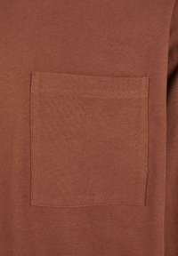 Camiseta de algodón marrón con un bolsillo en el pecho cosido. La tela tiene una textura suave con un diseño liso, sin patrones ni adornos.