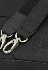 Schwarzes Lederarmband mit matter Textur, ausgestattet mit silbernen drehbaren Clips aus Metall und eingraviertem "BURKEY"-Logo auf einem glatten Hintergrund.