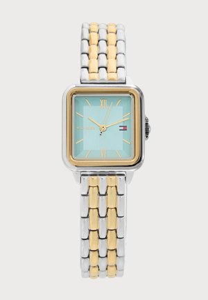 Square-faced wristwatch with gold and silver link band, light blue dial, gold Roman numerals, and small Tommy Hilfiger logo at 3 o'clock.