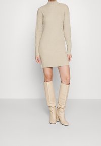 Beiges, geripptes Strickkleid mit langen Ärmeln und Mockkragen, kombiniert mit kniehohen, lässigen beigen Lederstiefeln.