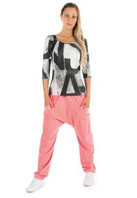 Långärmad topp med svarta abstrakta mönster på en vit bakgrund, som kombineras med löst sittande, rosa harembyxor och vita sneakers.