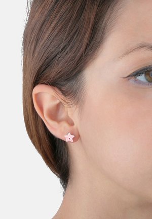 Orecchini a forma di stella in rosa e argento con tre pois bianchi, indossati all'orecchio di un modello. Design semplice con superficie liscia.