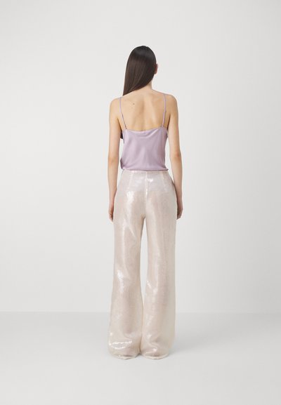 Camisola di raso lilla con spalline sottili abbinata a pantaloni ampi, lucidi e rosa chiaro ricoperti di paillettes. Il tessuto testurizzato crea un effetto riflettente.