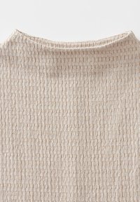 Beige textured fabric top with a ribbed design, featuring alternating narrow and wide patterns and a round neckline.