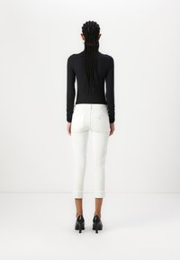 Maglietta nera a maniche lunghe abbinata a jeans bianchi scampanati. I jeans presentano orli ripiegati e sono completati da scarpe nere con tacco alto.